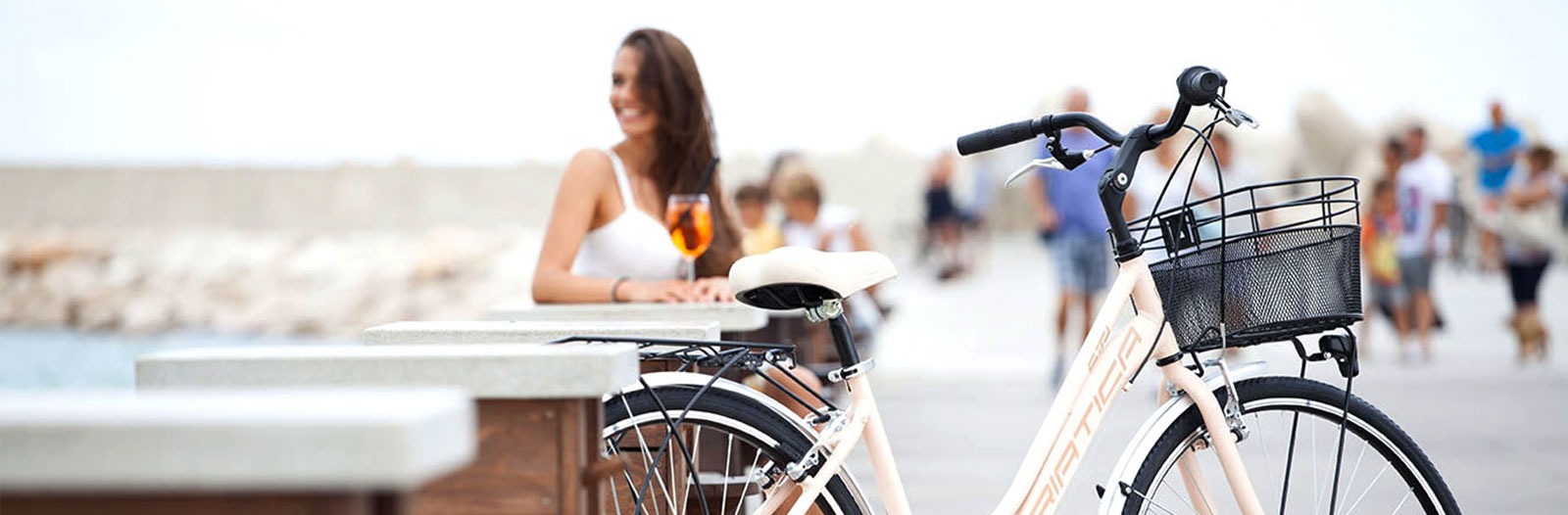 Bicicleta de cidade Adriatica cor-de-pêssego com cesto num passeio marítimo